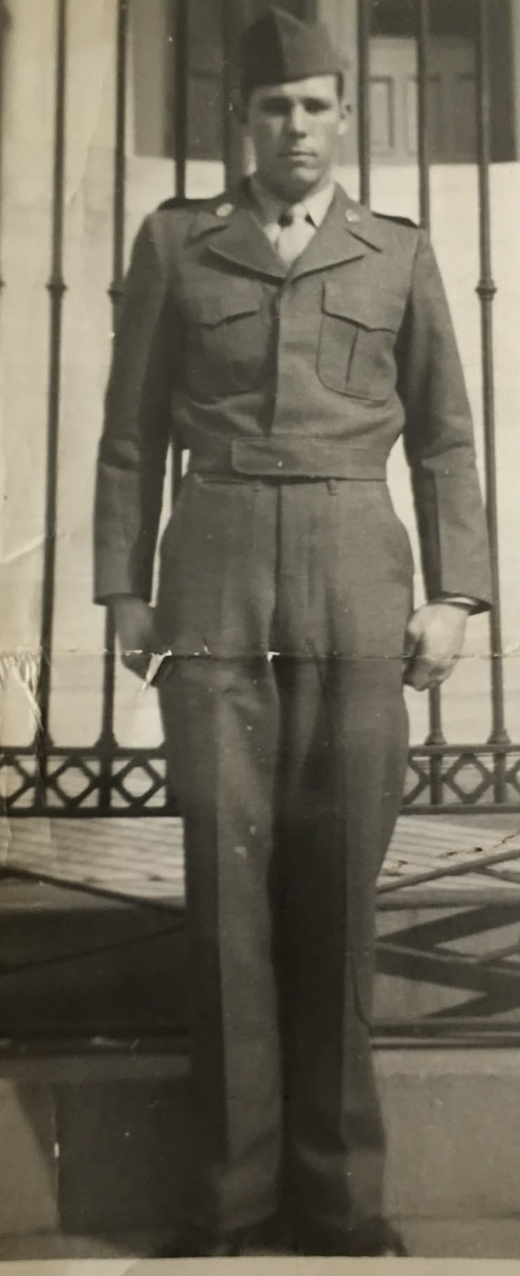A person in a military uniform standing outdoors in front of a fence.