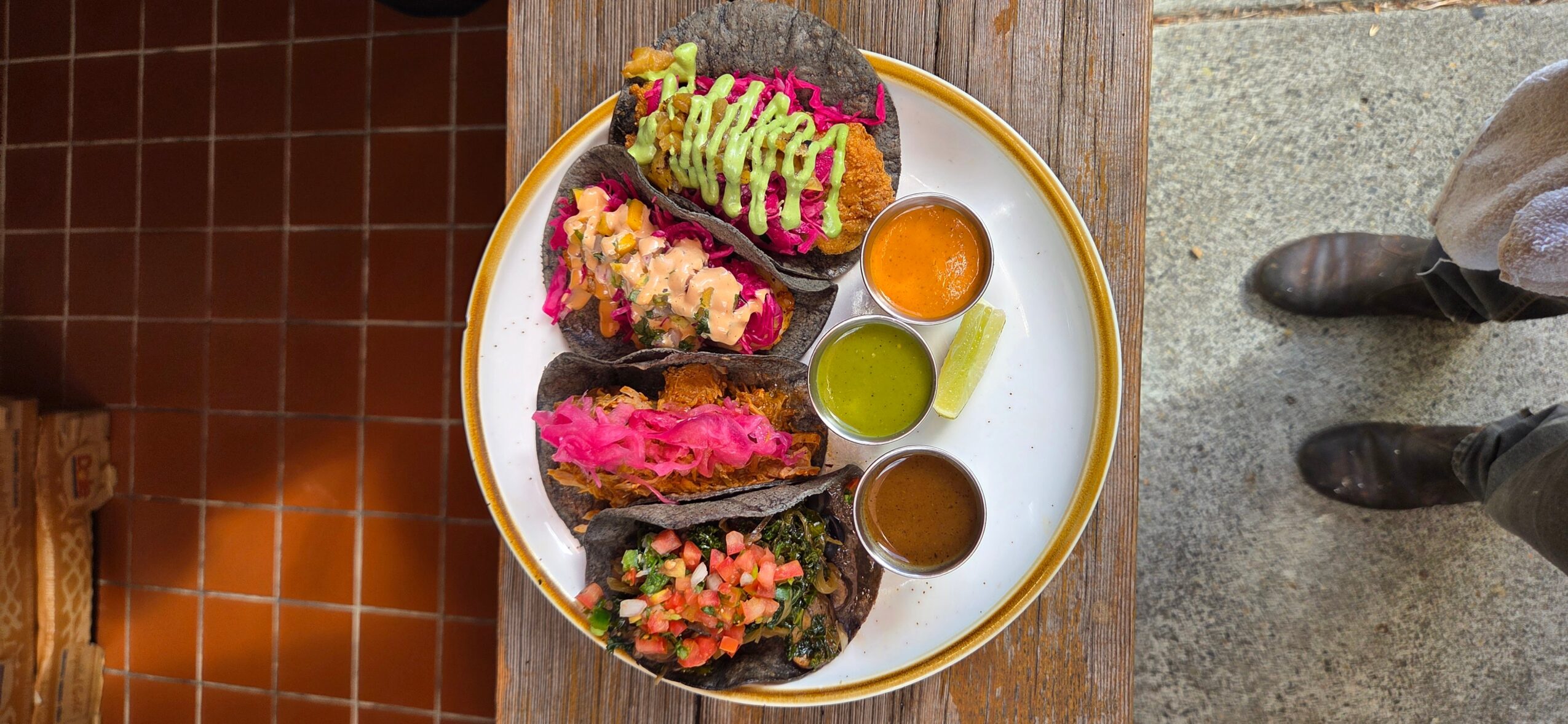 Plate with colorful desserts and small cups of sauces on a wooden table, viewed from above.
