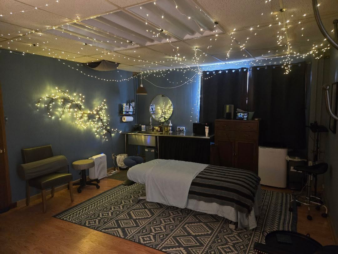 Room with massage table, string lights, chairs, and a globe, decorated with fairy lights and a patterned rug.