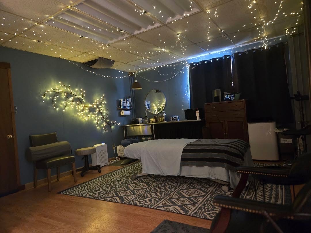 A room with a bed, chairs, and a desk, decorated with string lights on the ceiling and wall, and a globe on the desk.