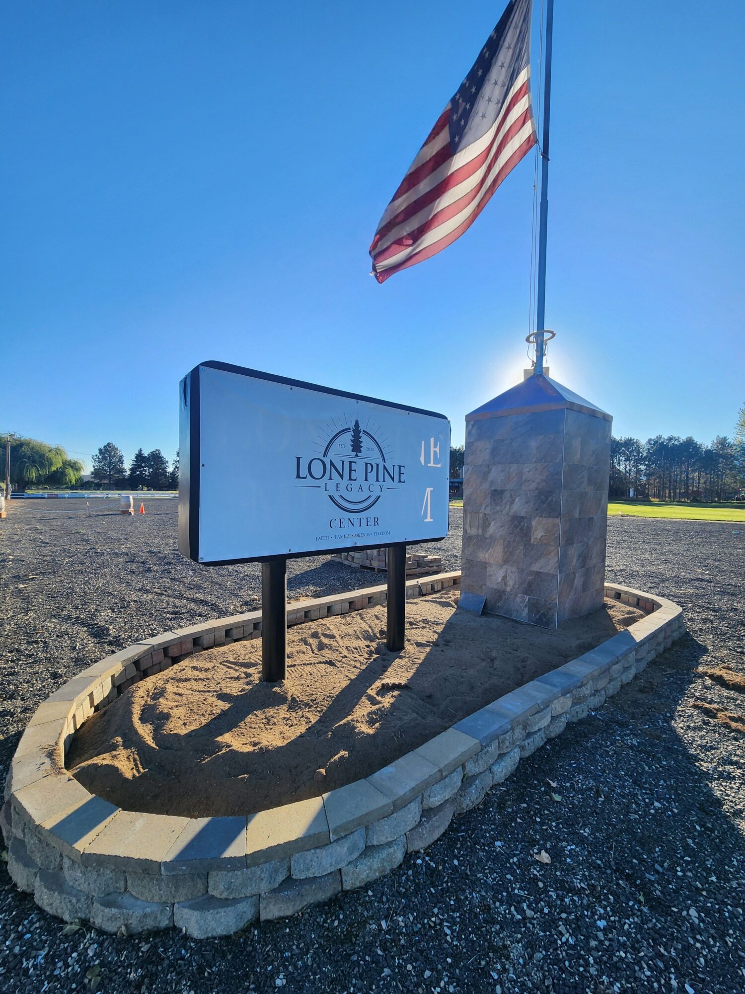 Flagpole with American flag and a sign for Longview, with a blue sky background.