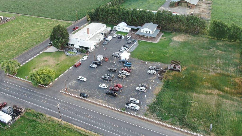 Aerial view of a parking lot with cars, adjacent to buildings and green fields.