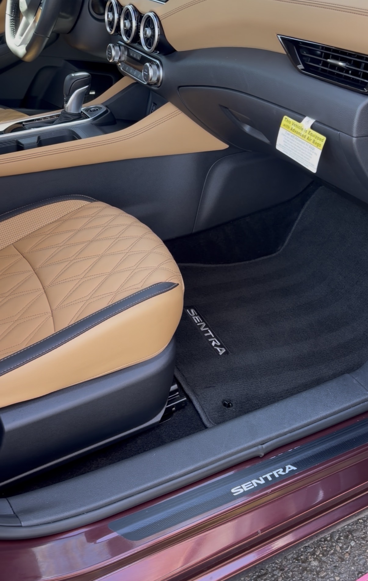 Car interior showing tan quilted seat, dashboard, and black floor mat with 'SENTRA' logo, no visible people or text.