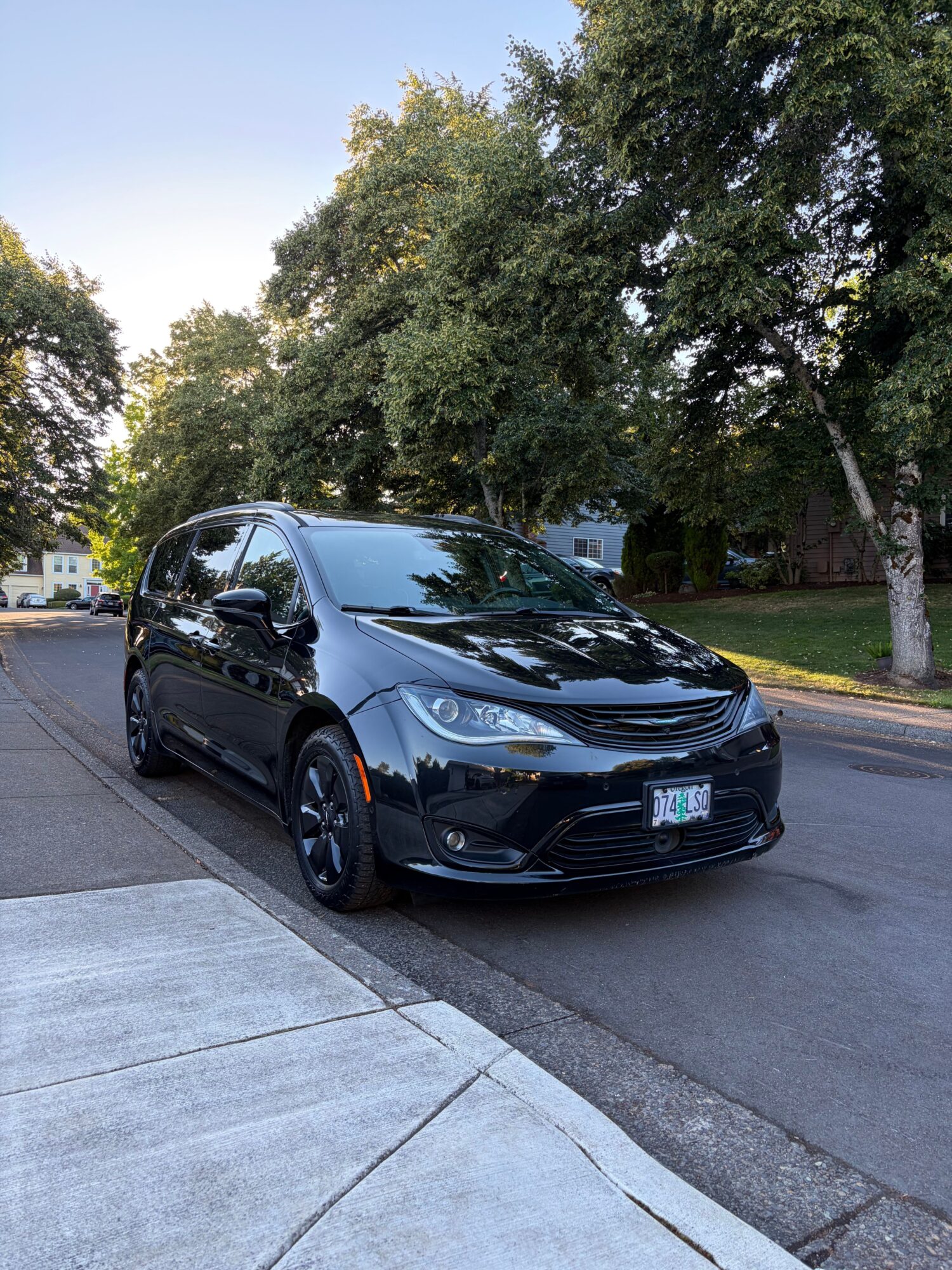 Black car parked on street with trees and sidewalk in background.