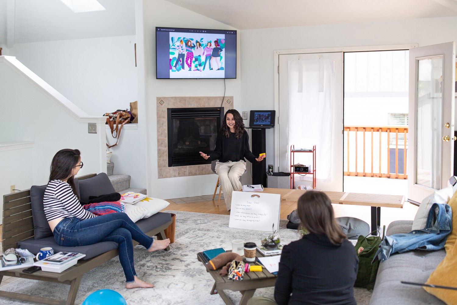 Group of people in a living room with a fireplace, TV, and balcony, engaged in a discussion or presentation.