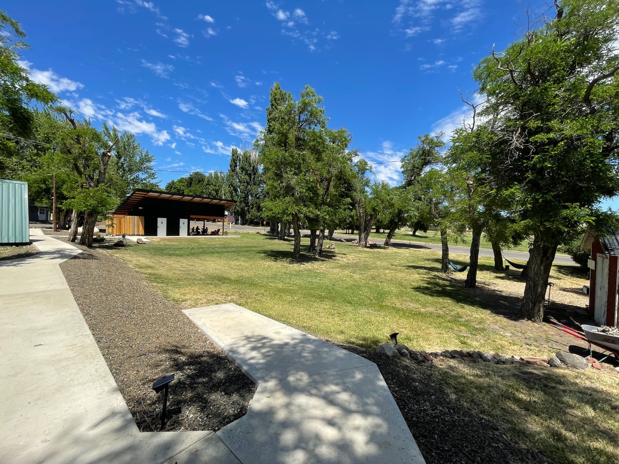 Open grassy area with trees, a building in the background, and a partly cloudy blue sky.
