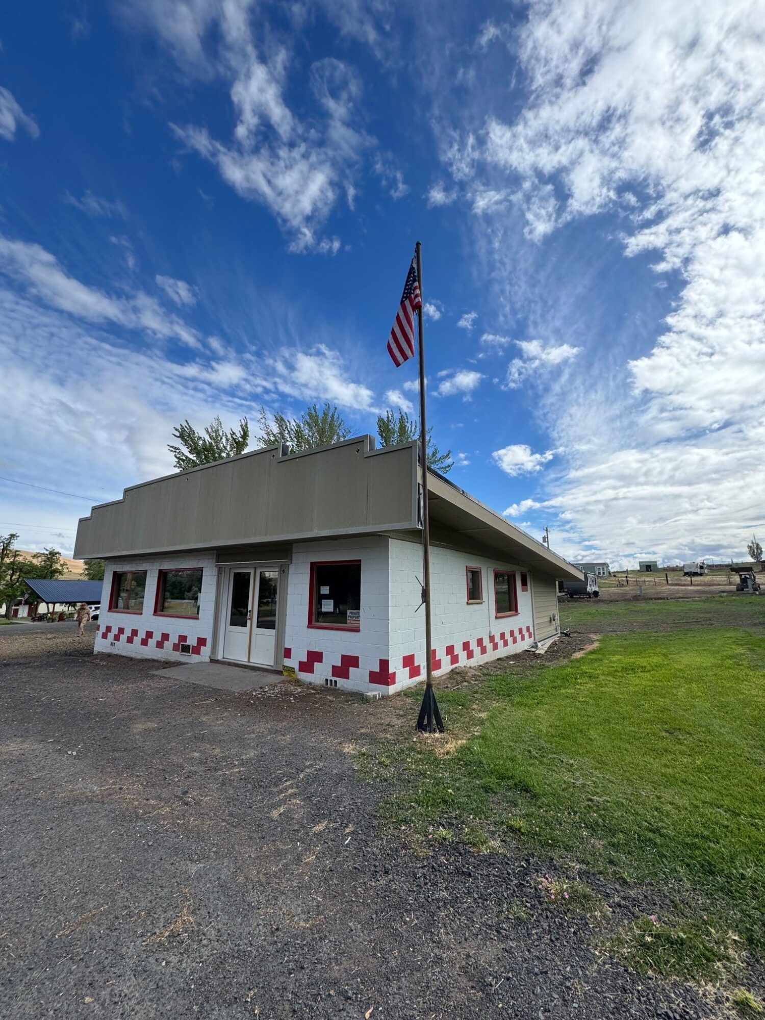 Small building with an American flag, red and white checkered pattern, and a grassy area, under a partly cloudy sky.