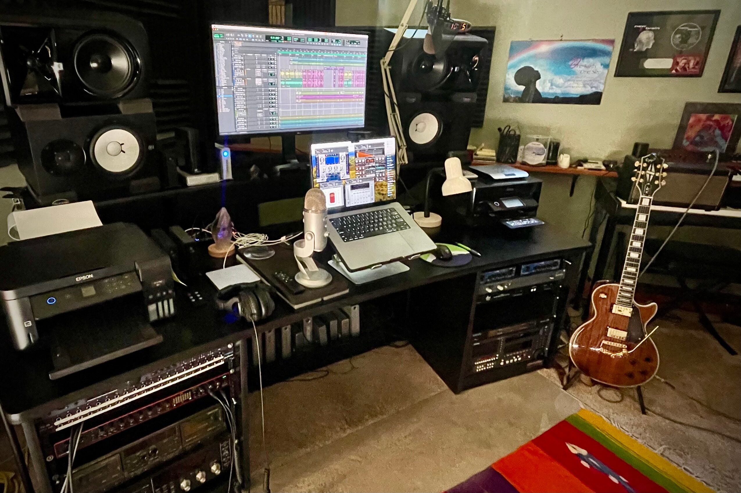 Music studio with computer, speakers, guitar, and artwork on the wall.