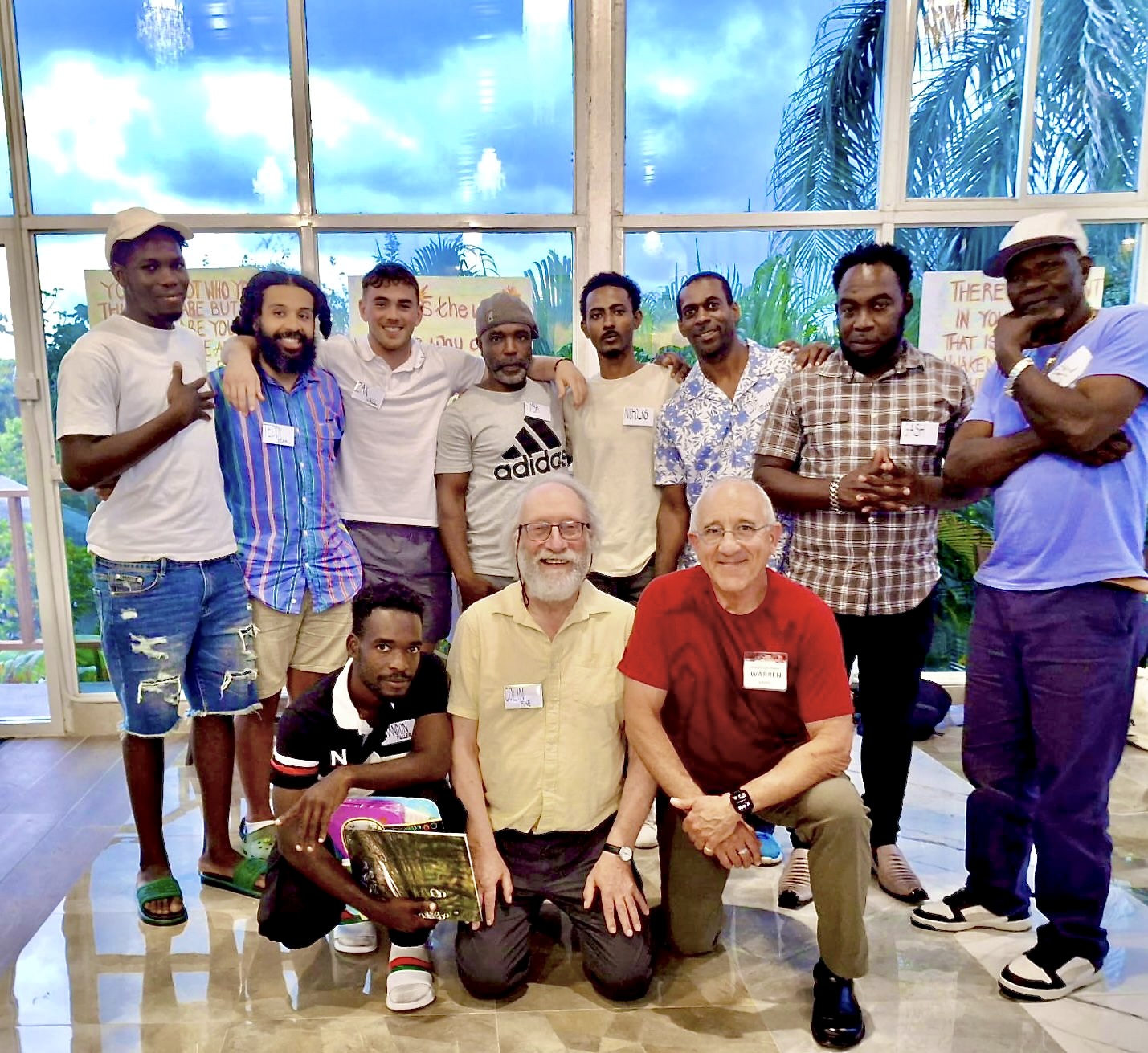 Group of people indoors with large windows, some standing and some kneeling, smiling and posing for a photo.