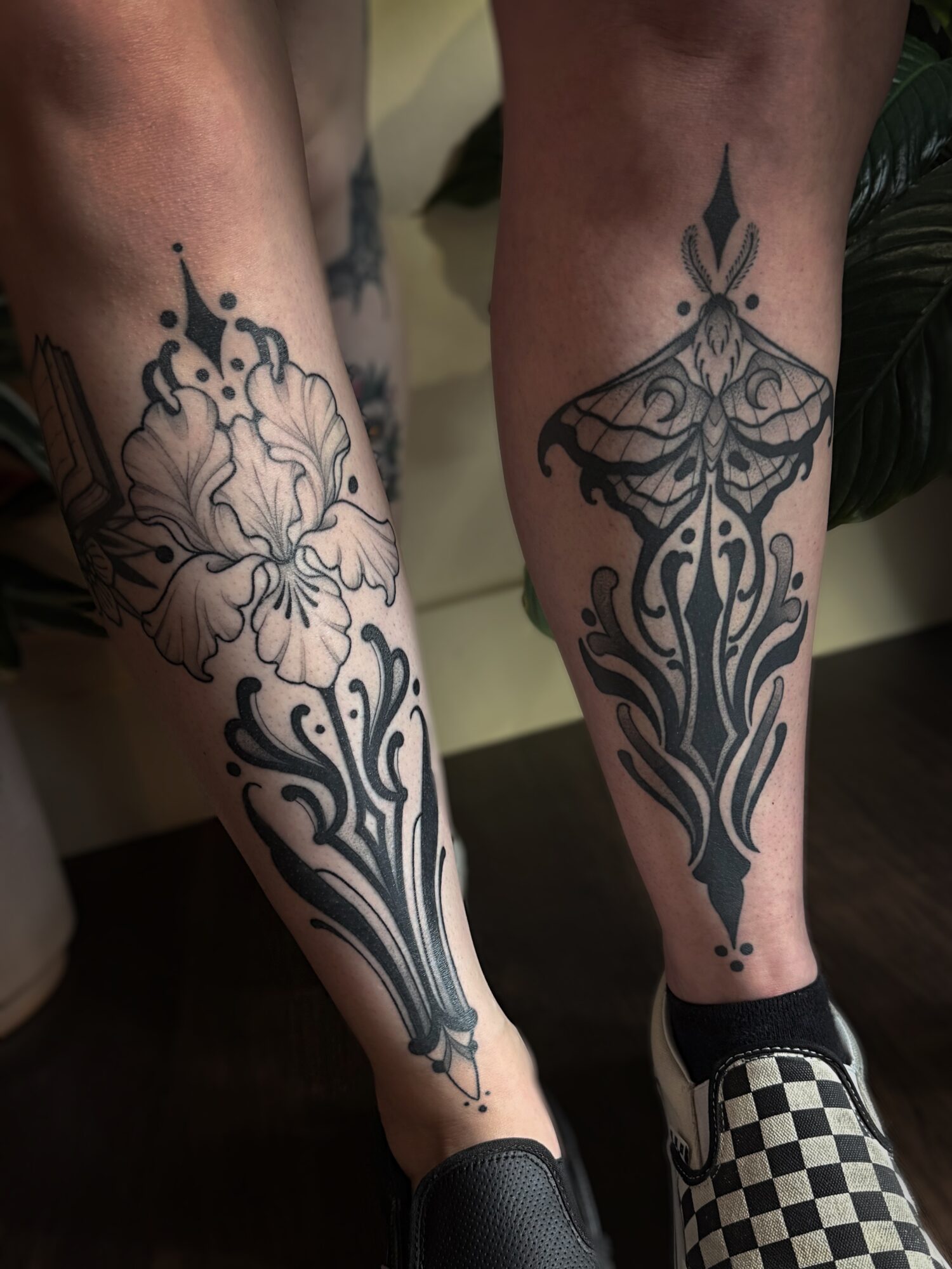 Two tattoos on lower legs with floral and abstract designs, one on each leg, in black ink.