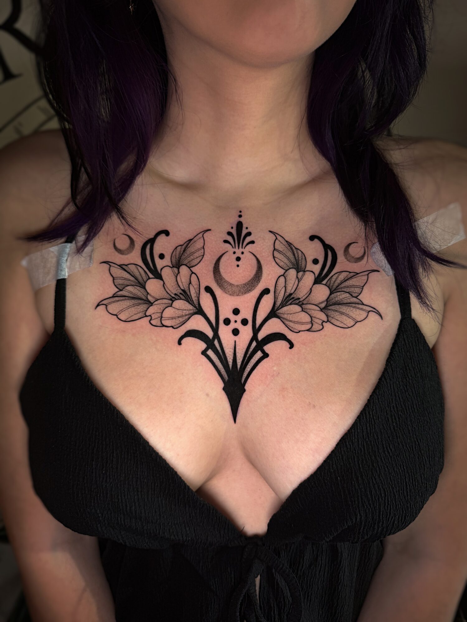 Person with a floral and geometric tattoo on chest, wearing a black top, dark hair visible.