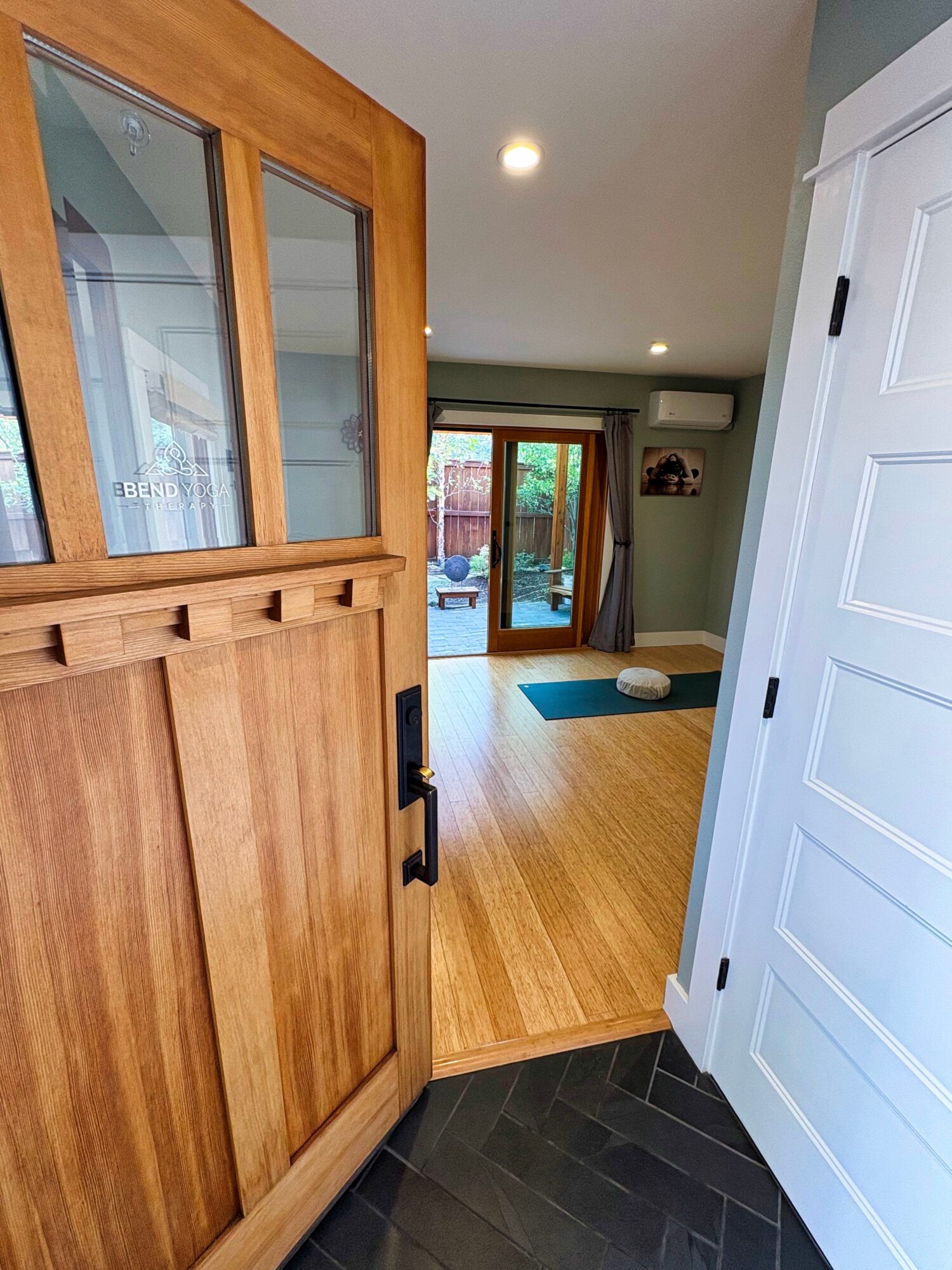 View of a living room with wooden flooring, sliding glass door, and a blue rug, seen from a doorway with a wooden cabinet.
