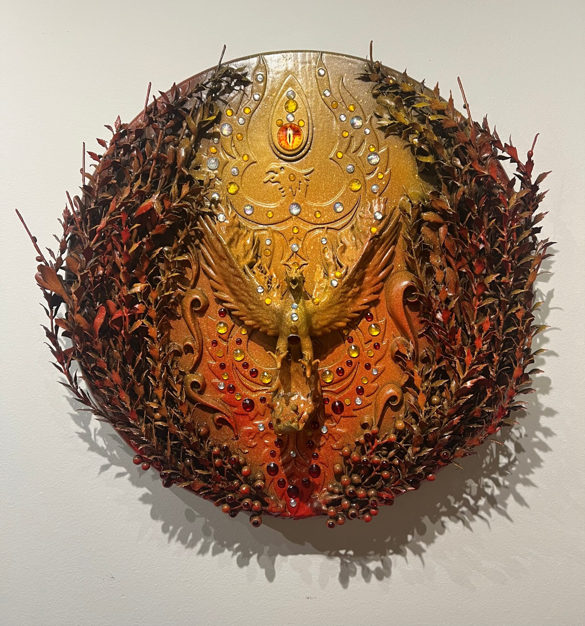Intricate circular artwork with detailed patterns, surrounded by reddish-brown foliage, featuring a central symmetrical design with yellow and orange hues.