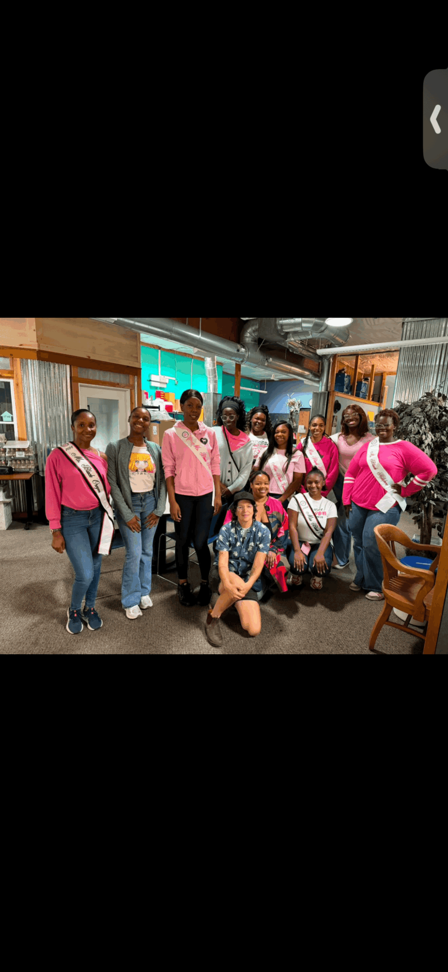 Group of people in pink shirts posing indoors, some standing and some kneeling, with a colorful background.