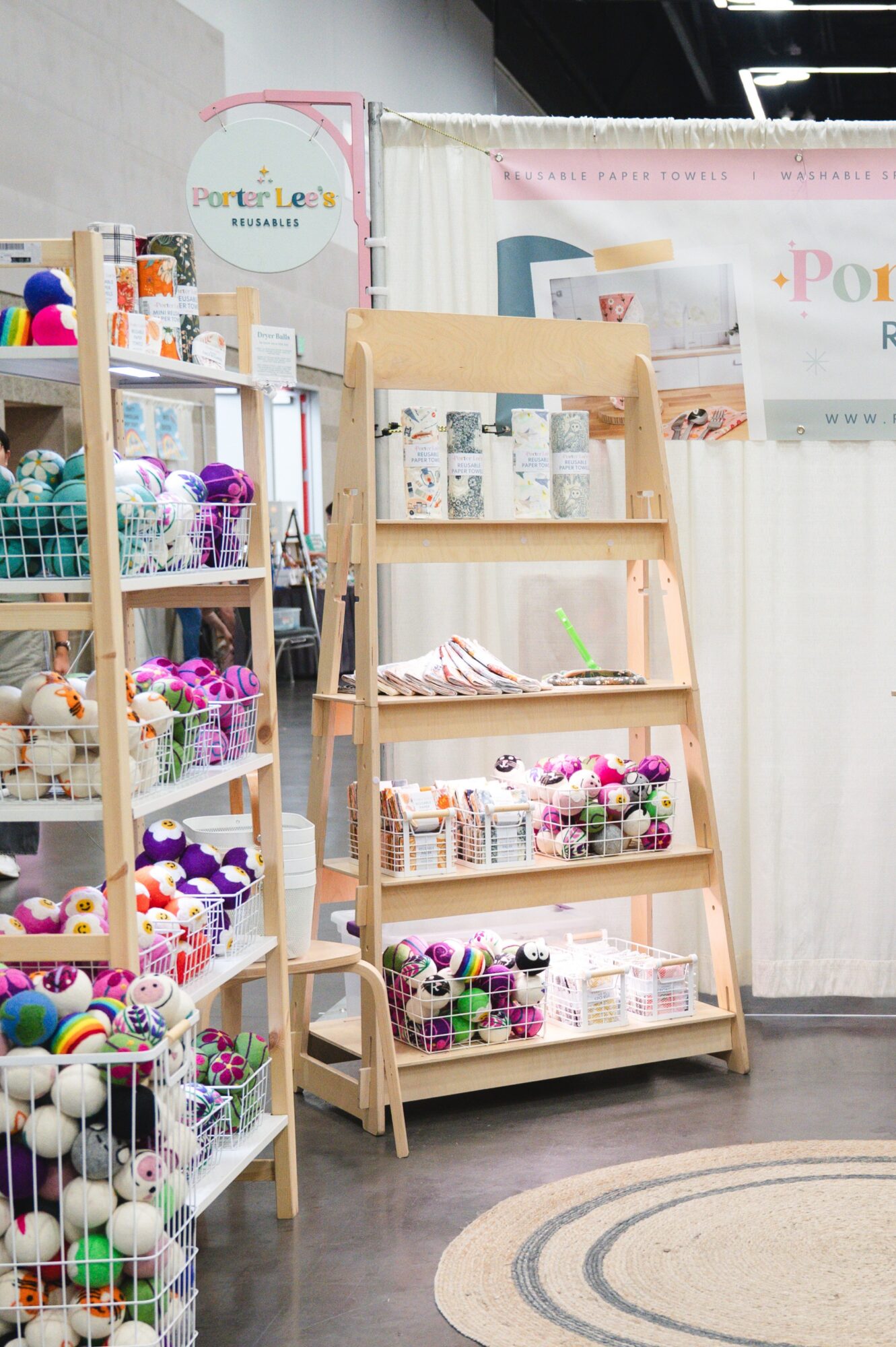 Wooden display shelf with flowers and craft supplies, surrounded by other shelves with colorful yarn and craft items, in a store.