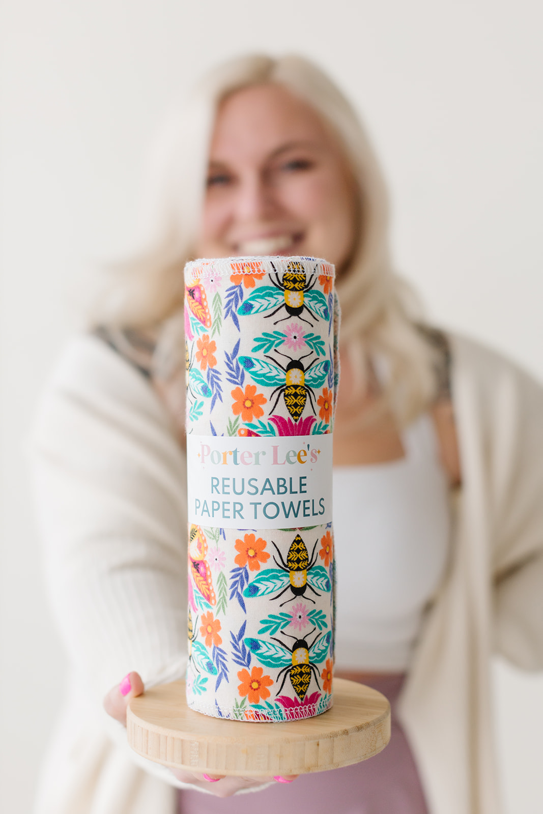 Blurry woman holding a colorful roll of reusable paper towels on a wooden stand, smiling.