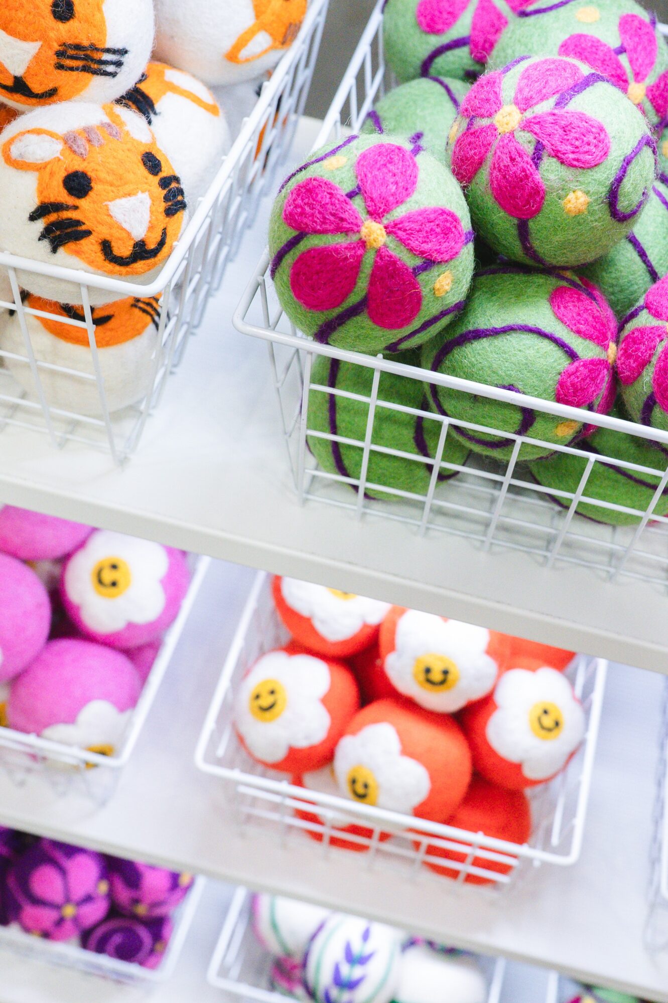Colorful plush toys with floral and animal designs in wire baskets on a white shelf.