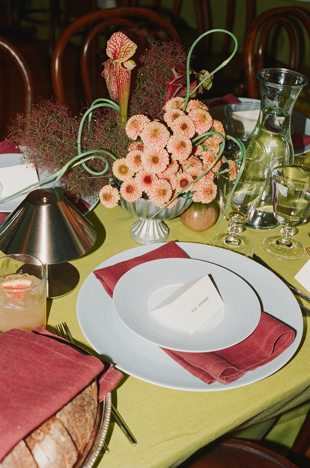 Table setting with a floral centerpiece, plates, glasses, and a red napkin on a yellow tablecloth.