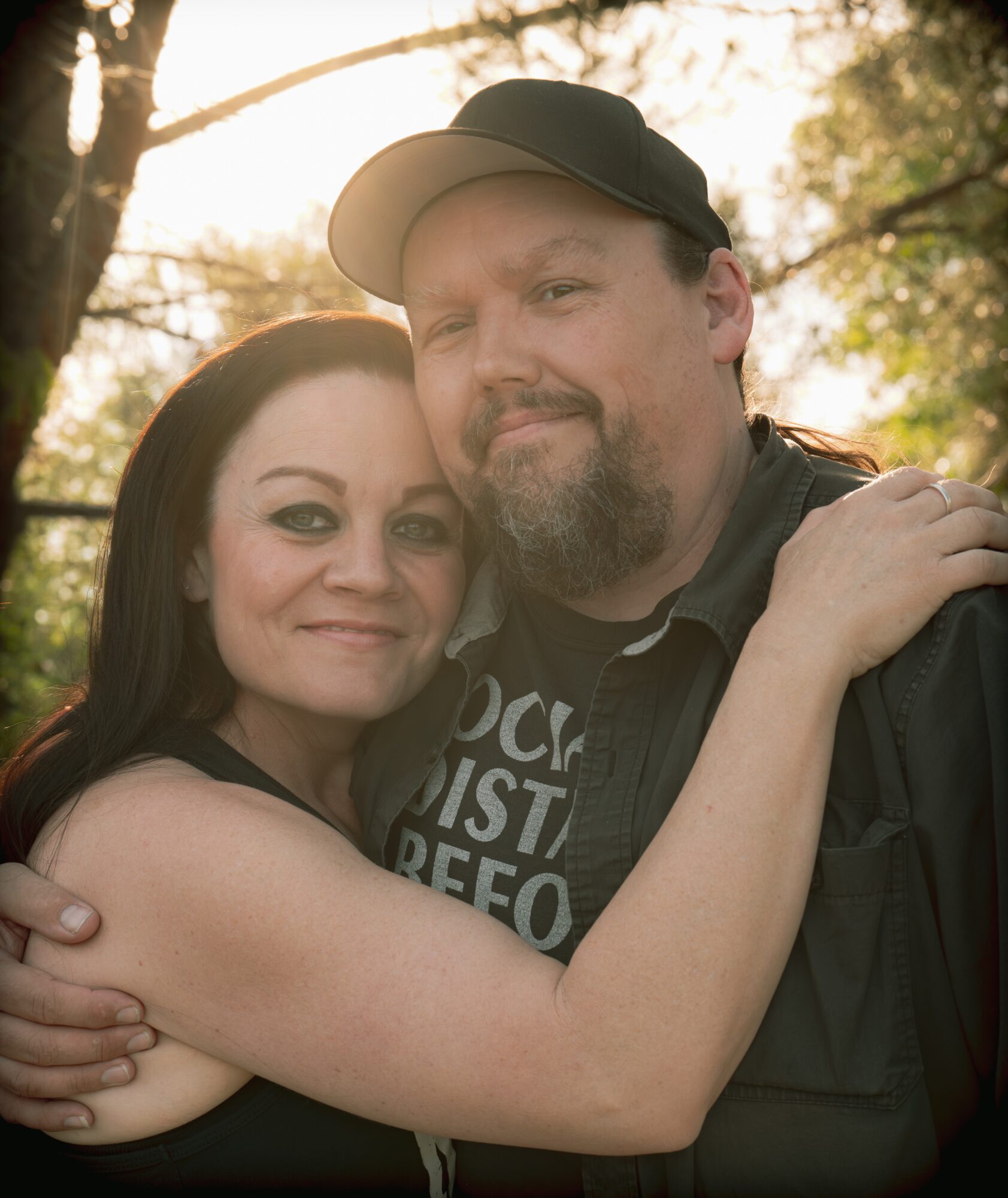 Two people hugging outdoors with trees and sunlight in the background.