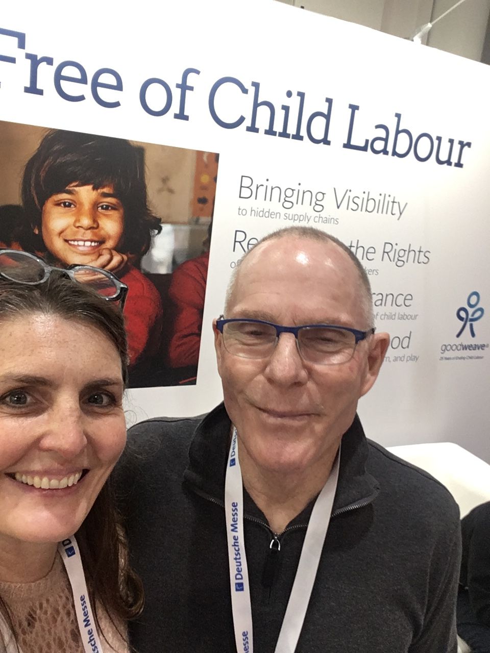 Two smiling people, one wearing glasses, in front of a banner with text about child labor and rights.