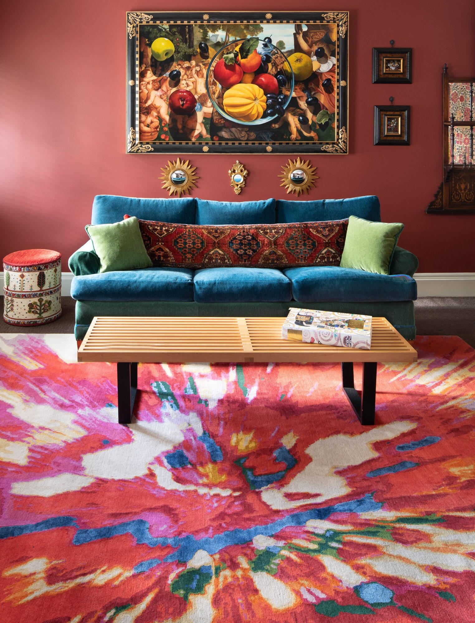 Living room with a blue sofa, colorful rug, wall art, and decorative pillows, against a red wall.