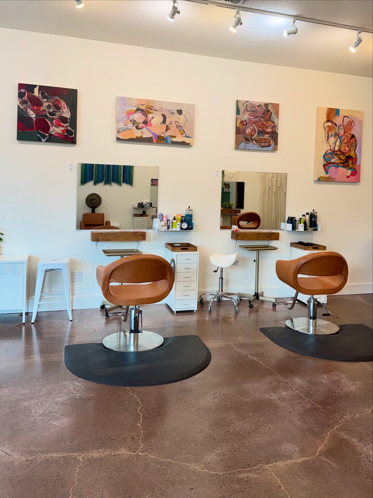 Hair salon interior with two styling chairs, mirrors, and colorful artwork on the wall.