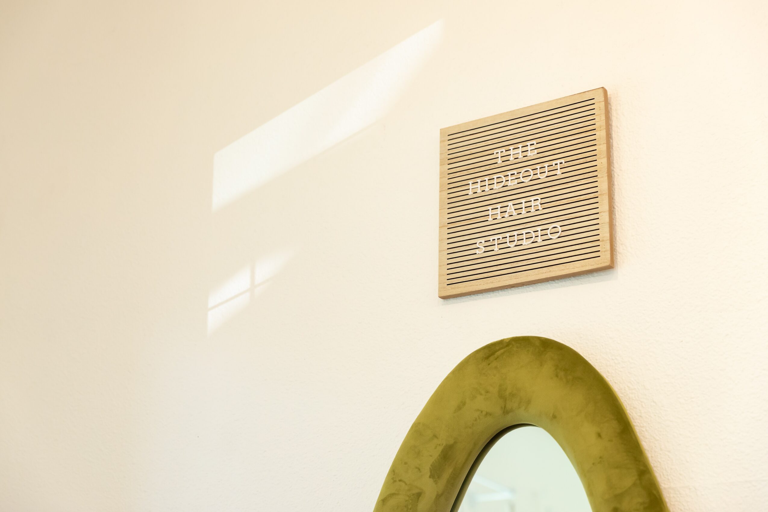 Wall with a framed message board and a mirror below it, illuminated by natural light.