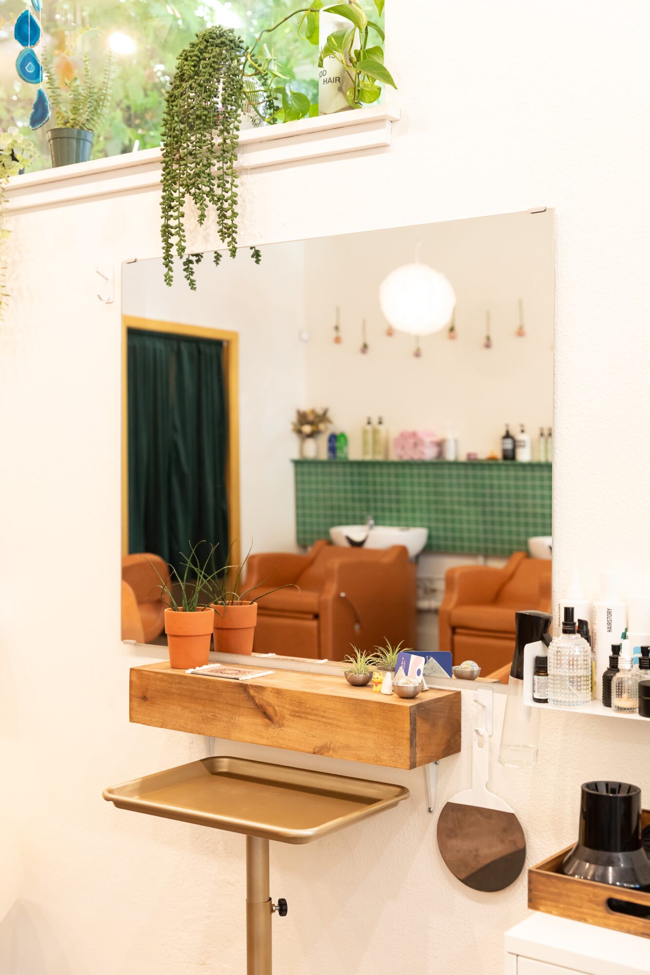 Interior of a cozy room with a wooden shelf, potted plants, and seating area with orange chairs and green wall, seen through a mirror.