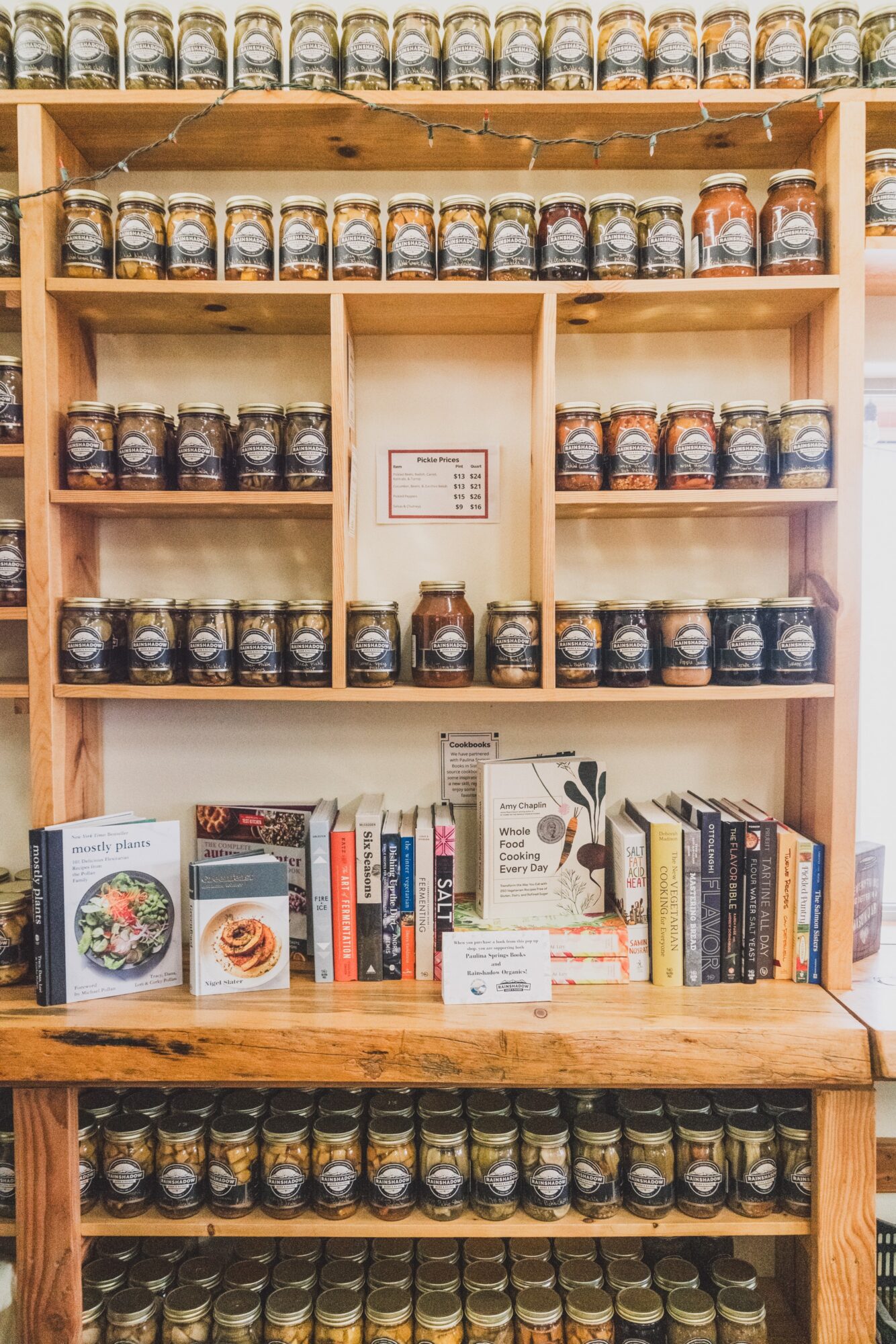 Wooden shelf with spice jars on top and books on the bottom, organized in sections, with a small sign in the middle.