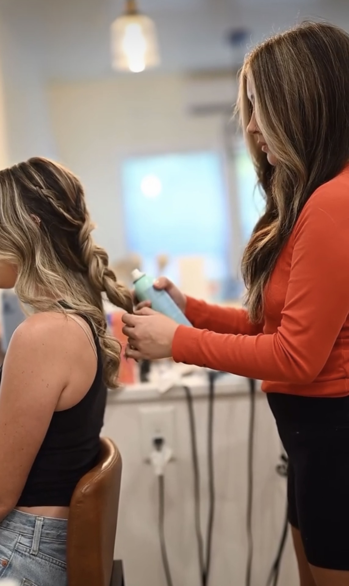 Person styling another person's hair in a salon, with a blurred background and natural lighting.