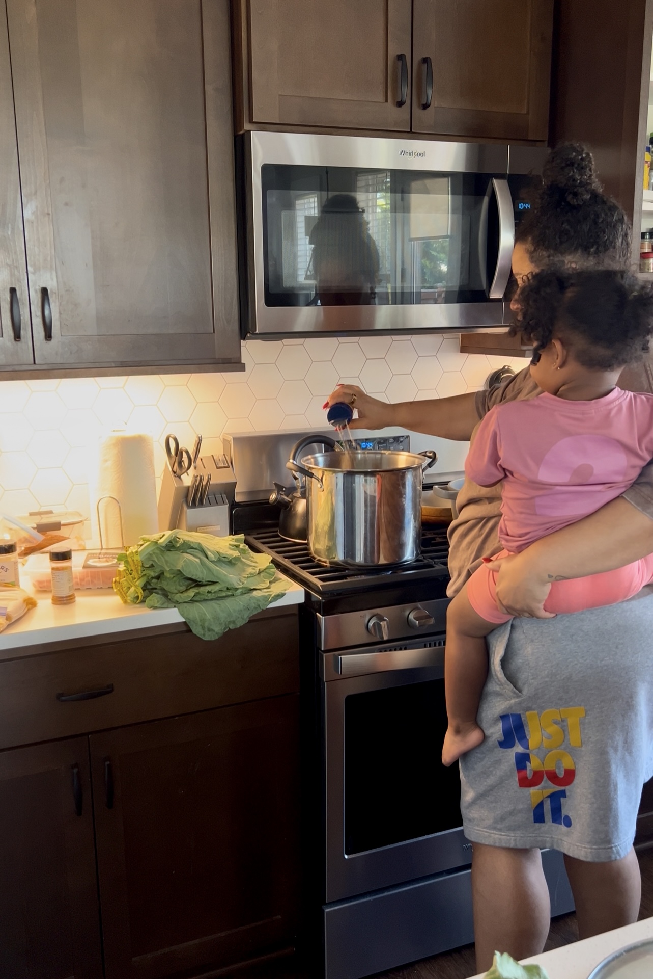 Child being held by an adult near a stove with a pot, in a kitchen with wooden cabinets and a microwave above.