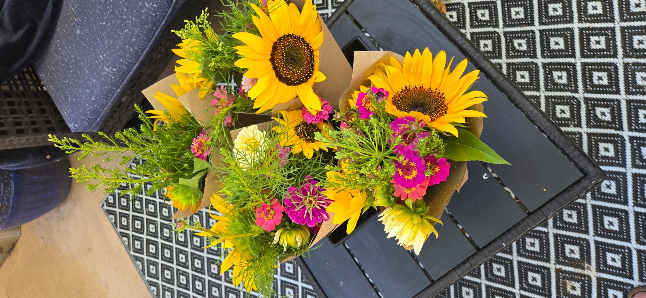 Bouquet of sunflowers, pink, white, and green flowers on a black surface.
