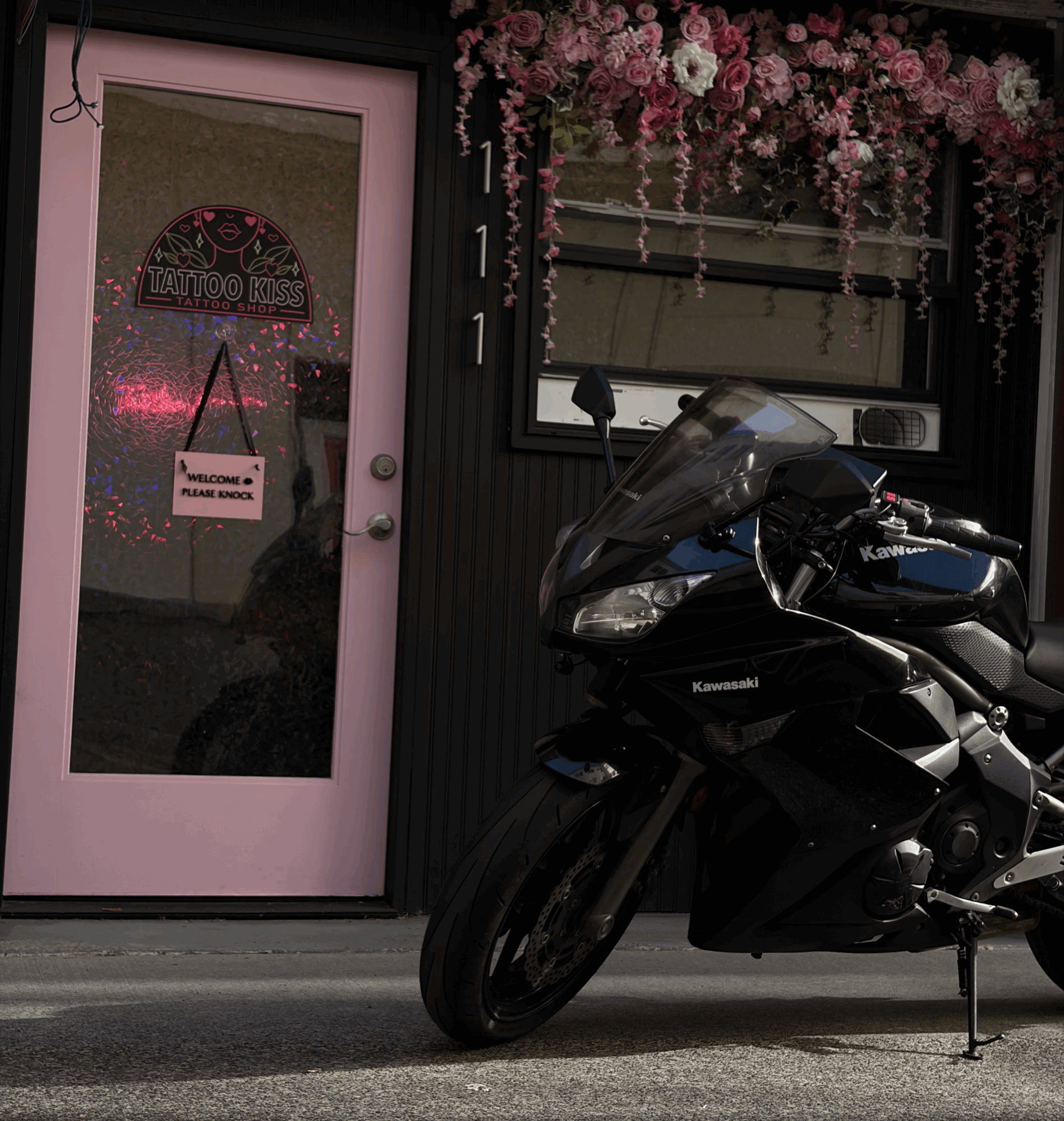Black motorcycle parked outside a building with a pink door and floral decorations above the window.