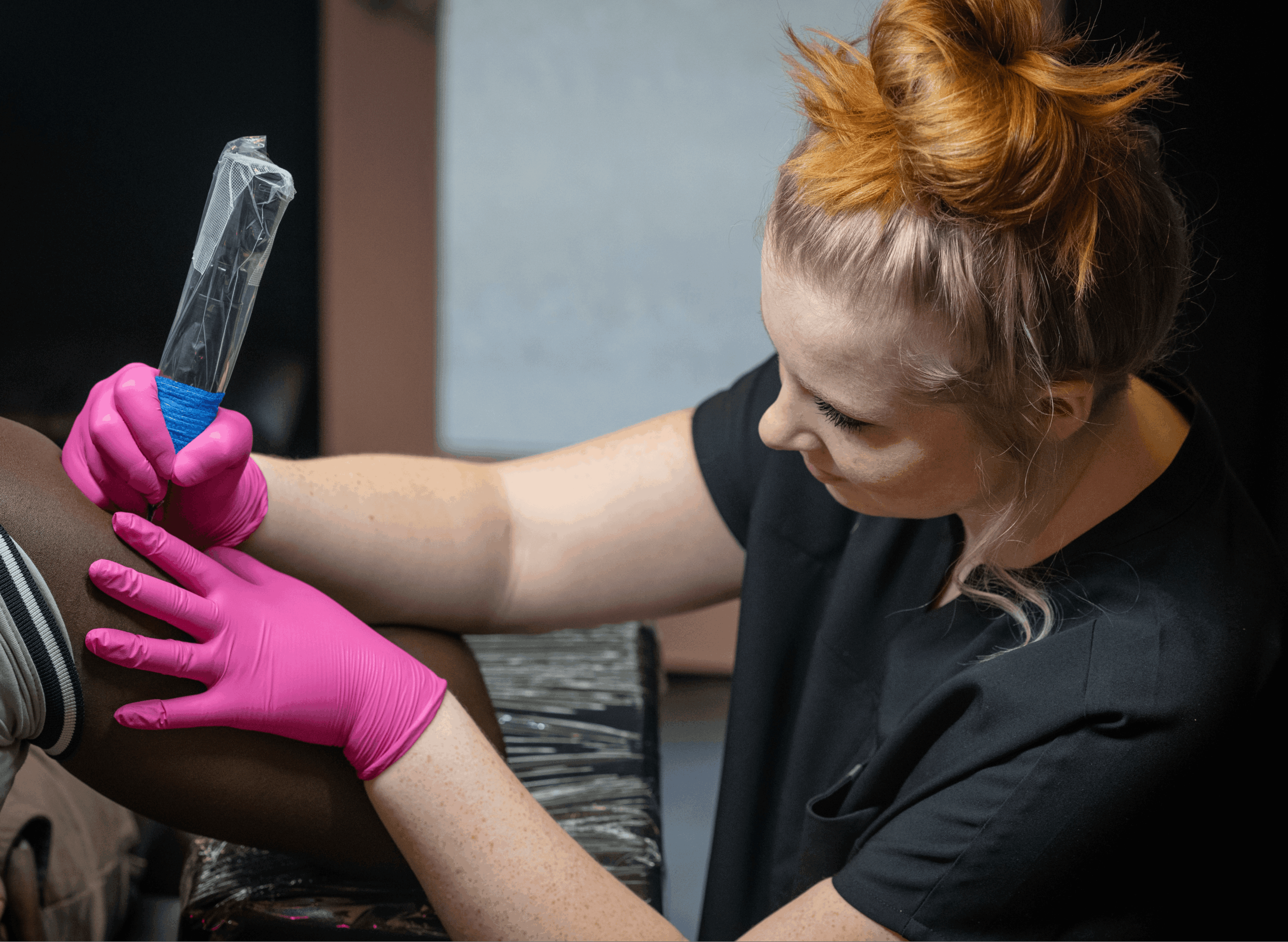 Person wearing pink gloves holding a syringe, preparing an injection on a person's arm, with a focused expression.