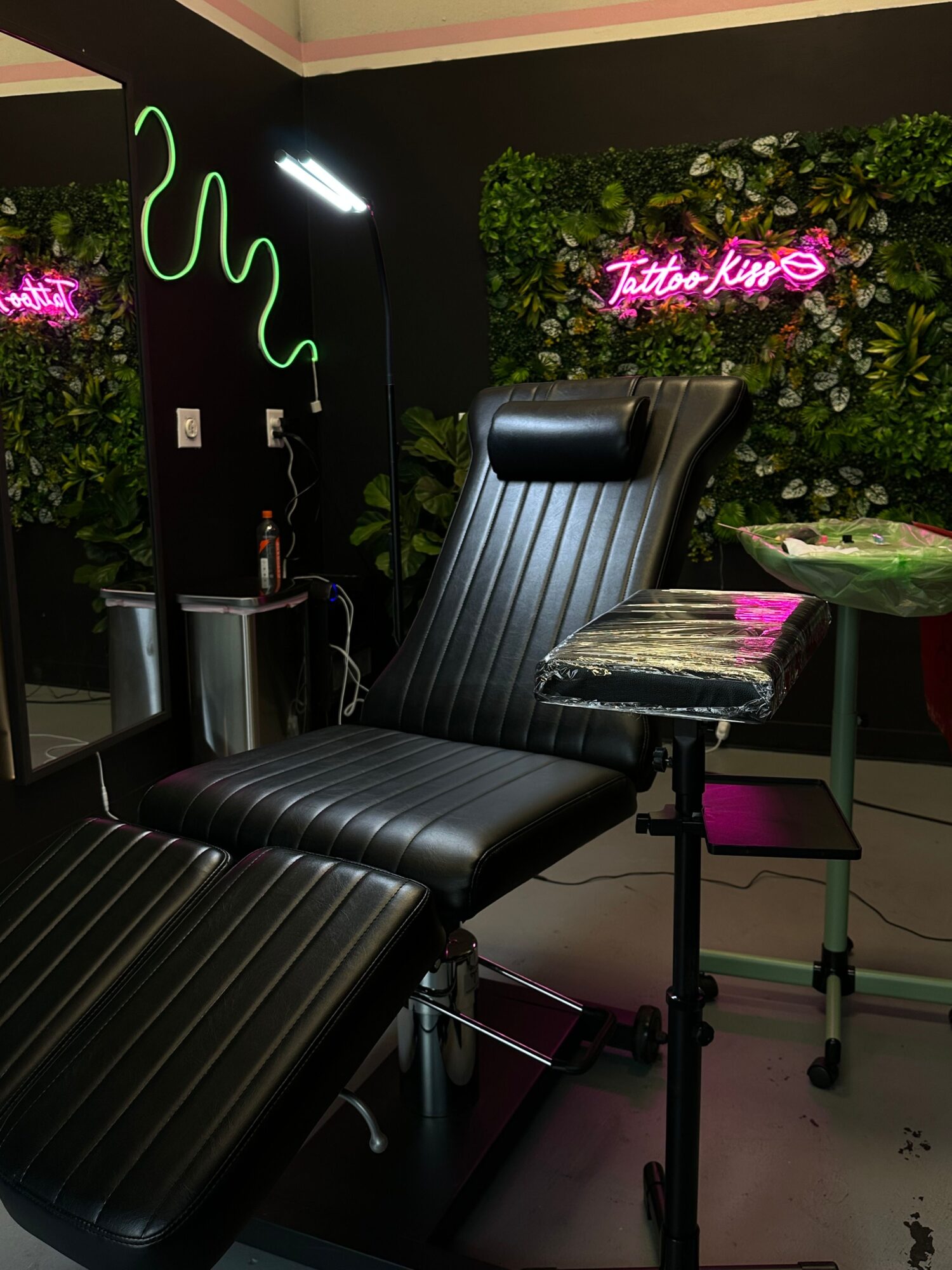 Salon chair with a mirror, neon sign, and green plant wall in the background.