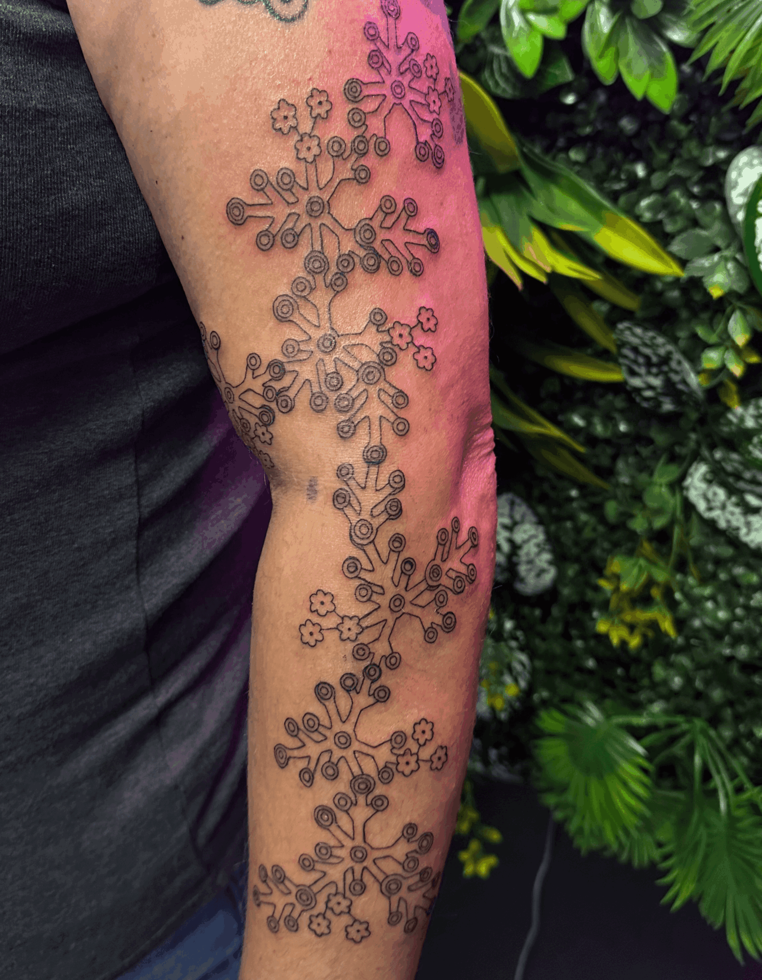 Tattoo of interconnected snowflakes on person's arm, with green foliage background.