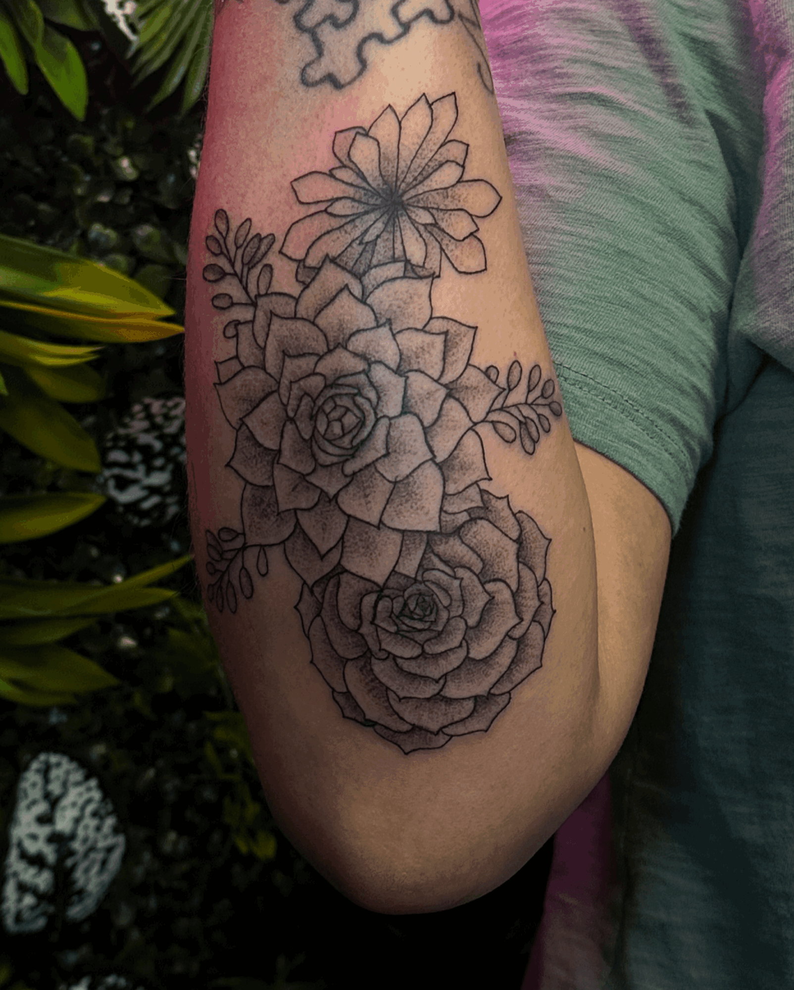 Tattoo of various flowers and leaves on a person's arm, with detailed line work and shading.