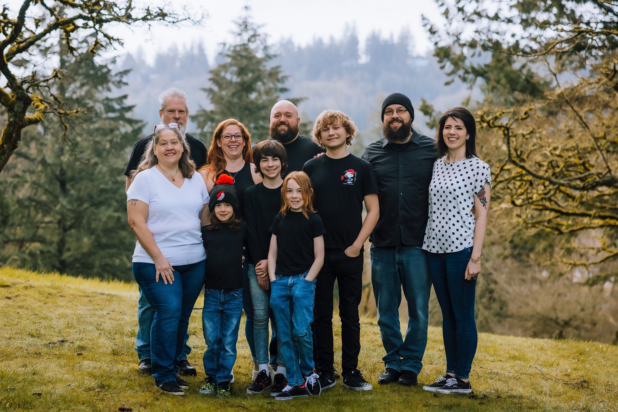 Group of ten people standing outdoors on grass with trees and hills in background.