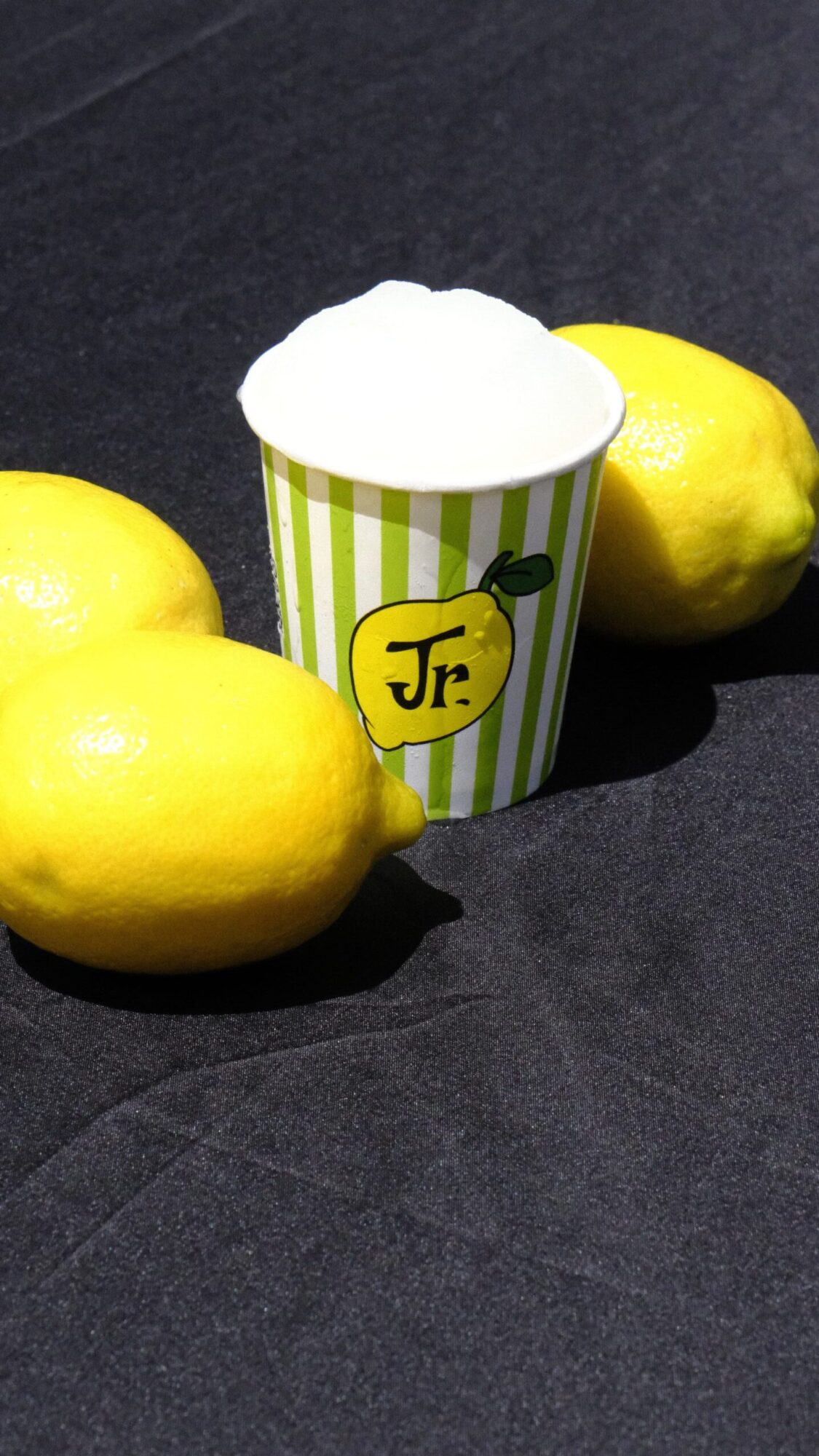 Two yellow apples and a striped paper cup with a yellow label on a dark surface.