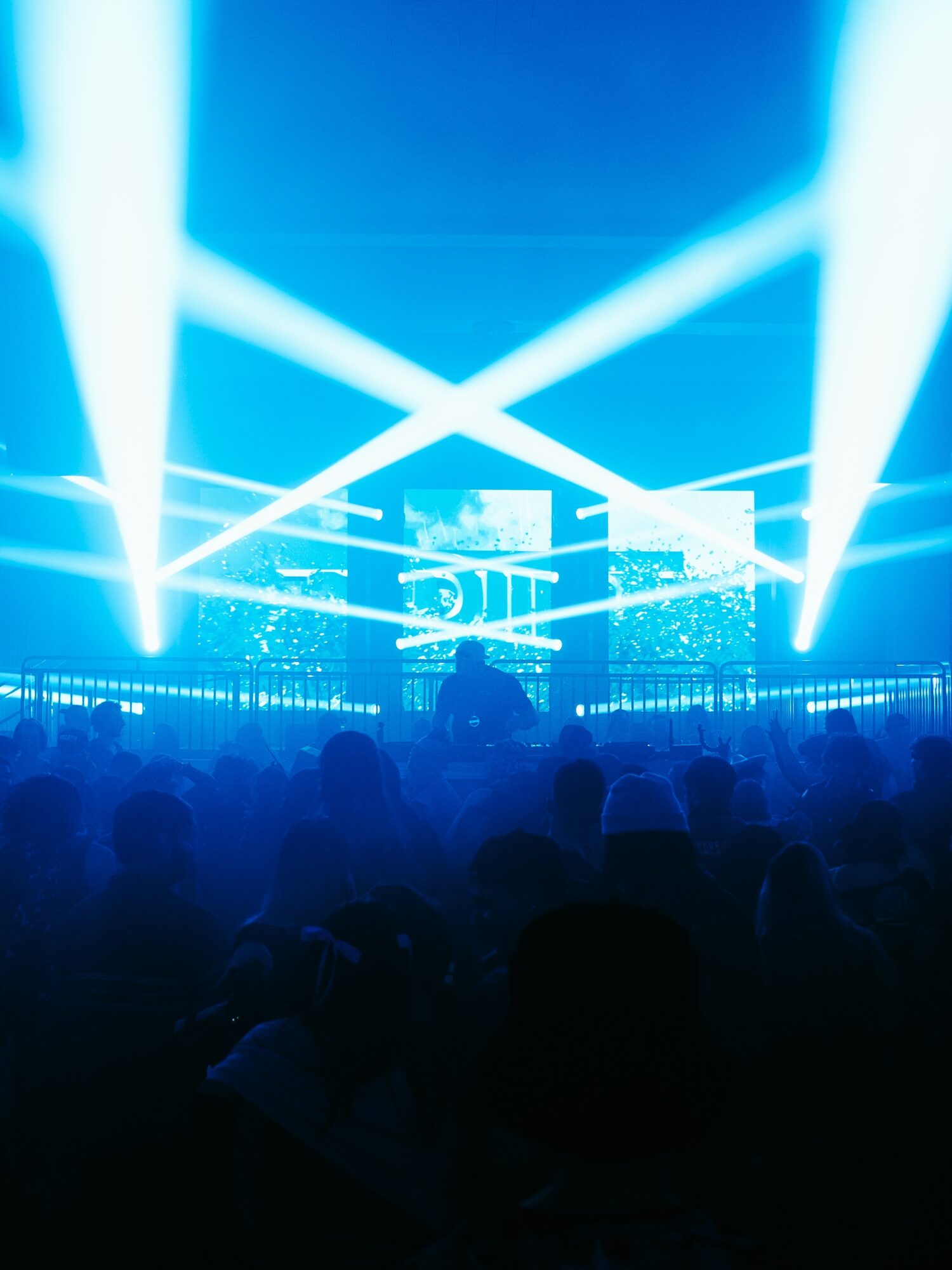 Concert scene with bright blue stage lights and silhouettes of audience members, electronic screens in background