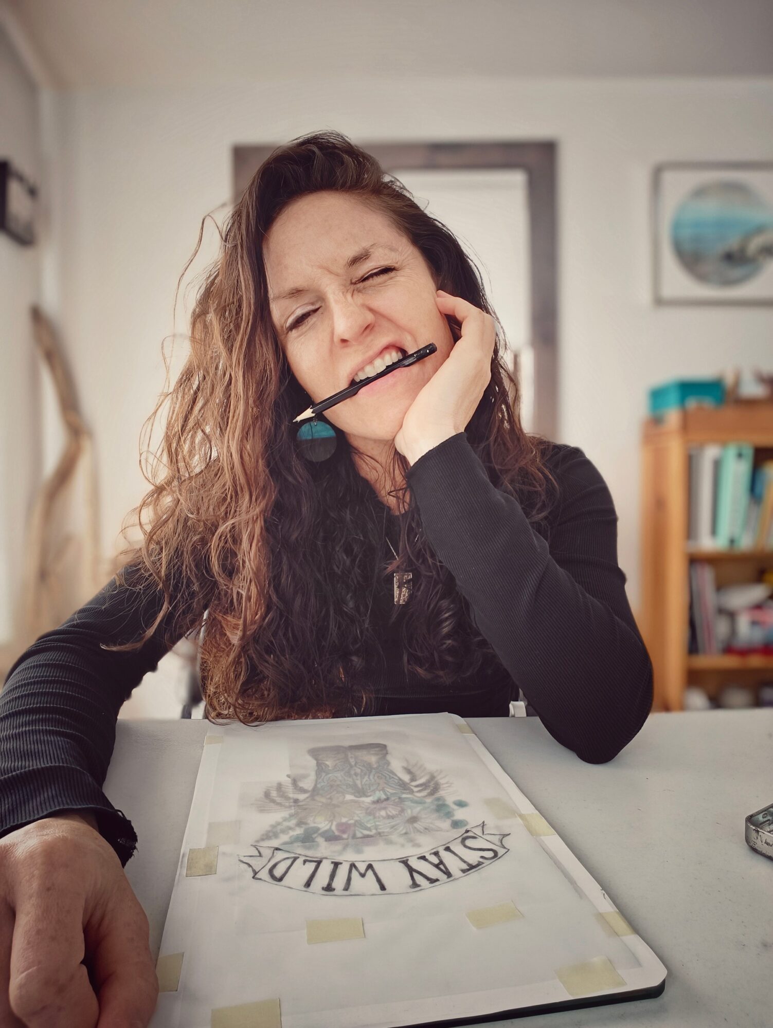 Woman with curly hair wearing a headset, smiling and resting her head on her hand at a desk.