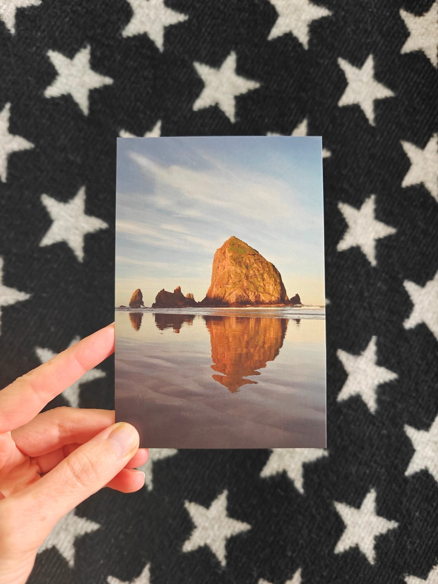 Person holding a photo of a large rock formation reflected in water, with a sky background, against a star-patterned fabric.