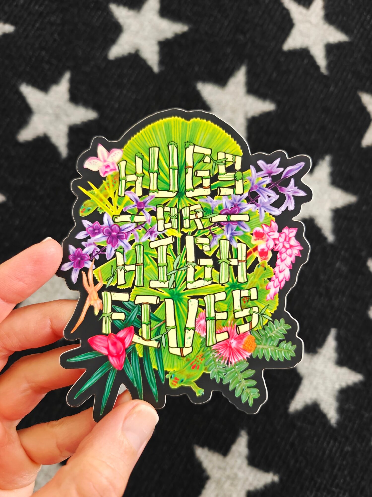 Colorful sticker with tropical plants, flowers, and the text 'HUGE MISTAKE' in bold letters, held by a hand.