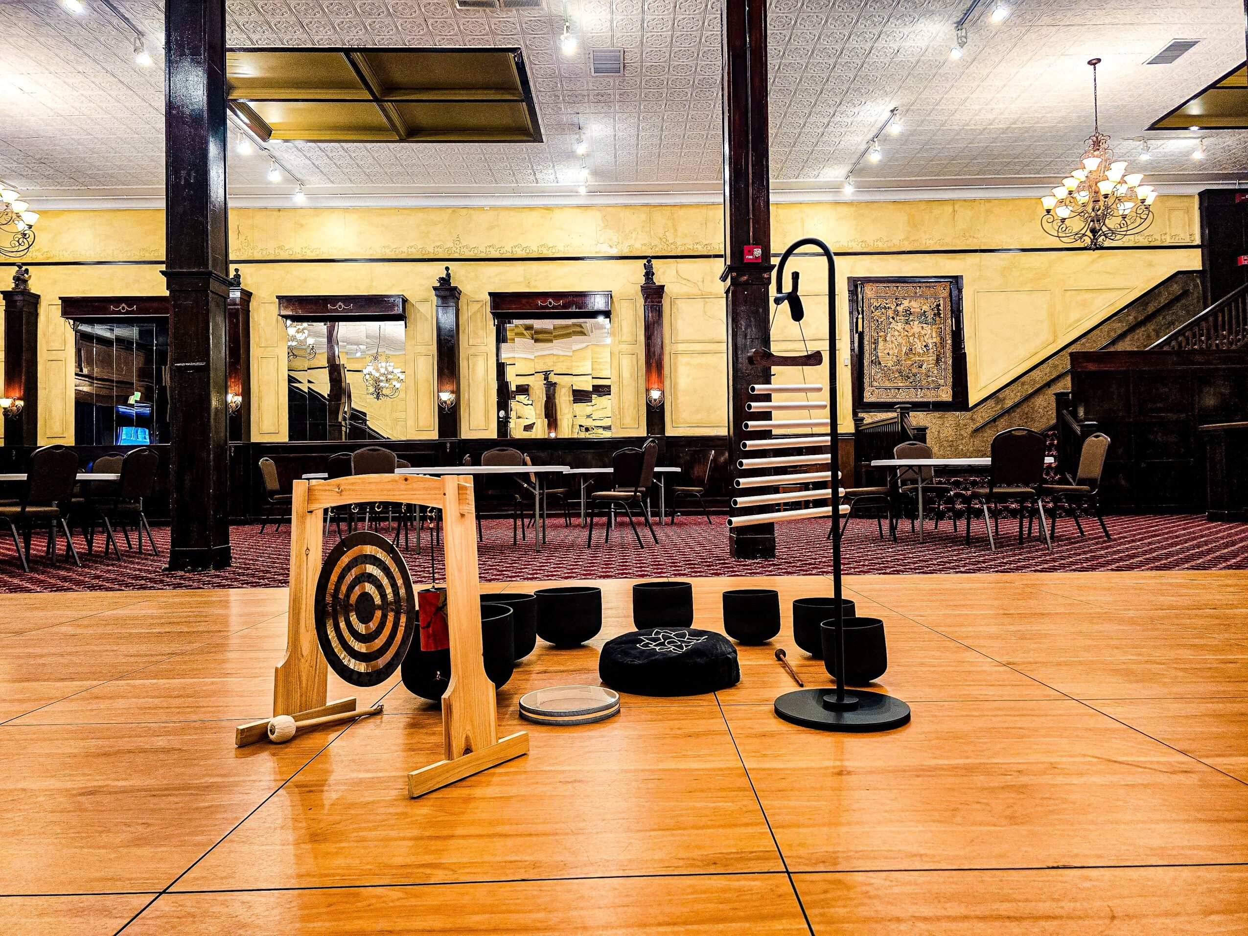 Stage with musical instruments and equipment in a room with yellow walls and chandeliers, viewed through a window. Word count: 20