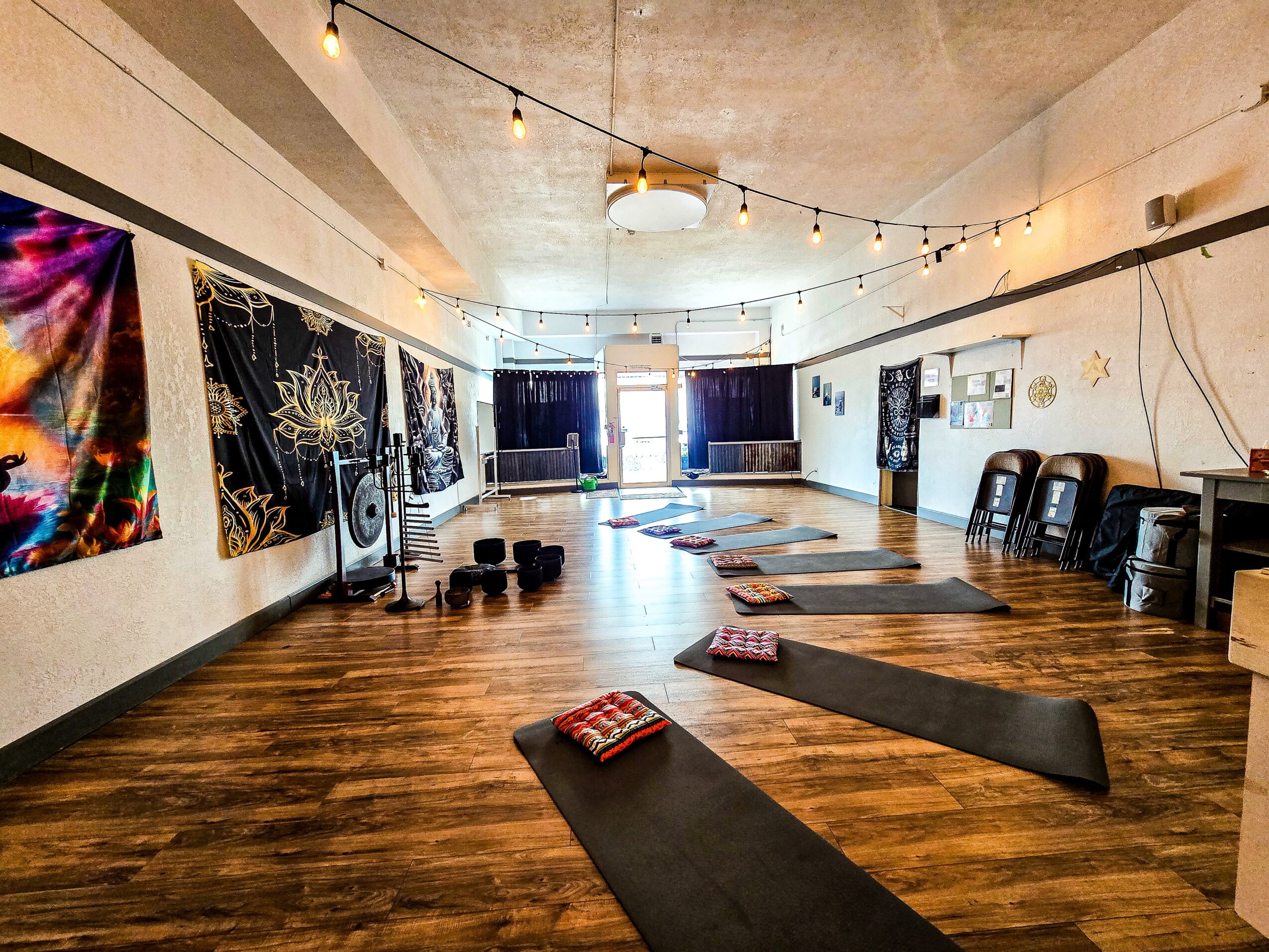 Yoga mats and blocks arranged in a spacious room with artwork on walls and string lights overhead.