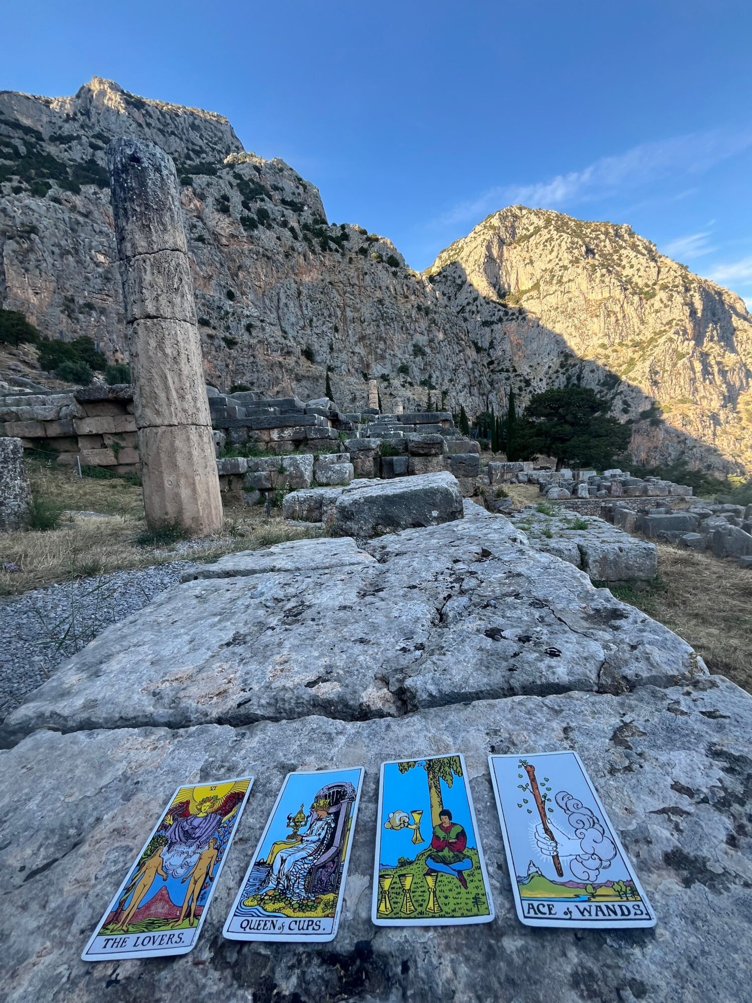 Four tarot cards laid on a rocky surface outdoors with mountains in the background.