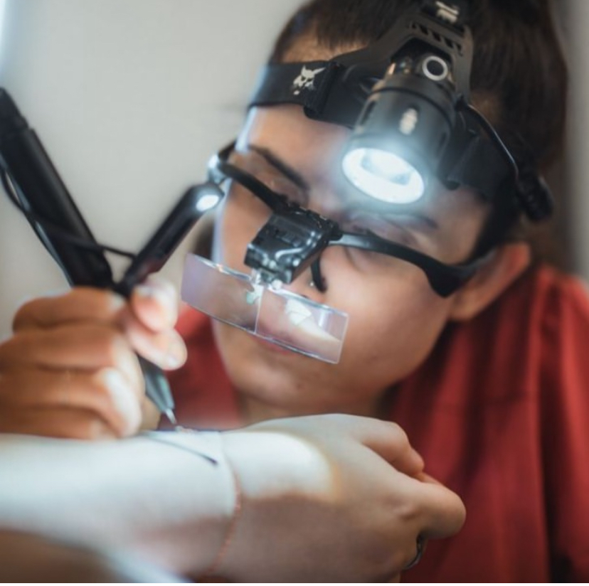 Child wearing a headlamp and magnifying glasses, closely examining an object with a pen, in a focused activity.