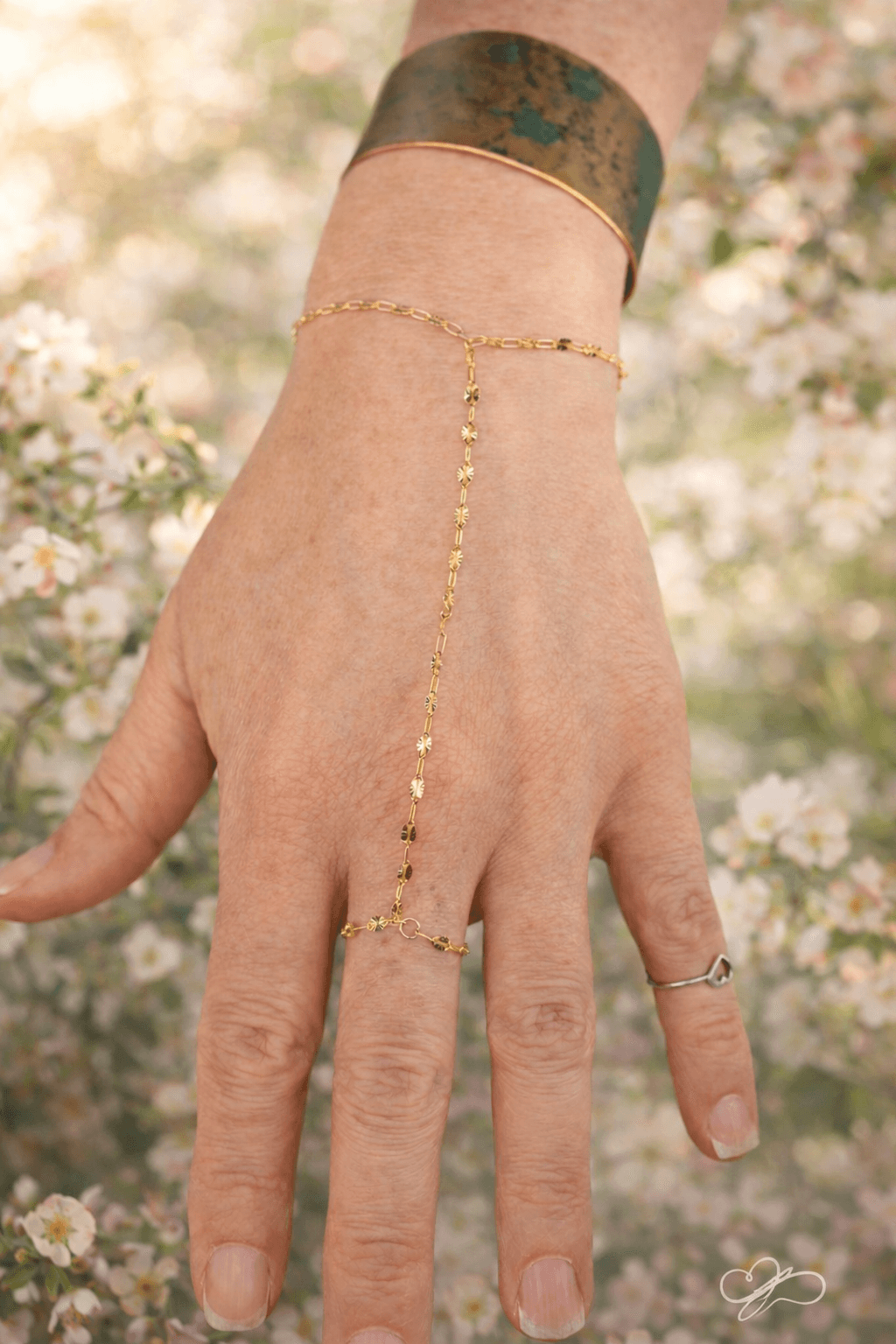 Close-up of a hand with jewelry, outdoors with blurred flowers in background.
