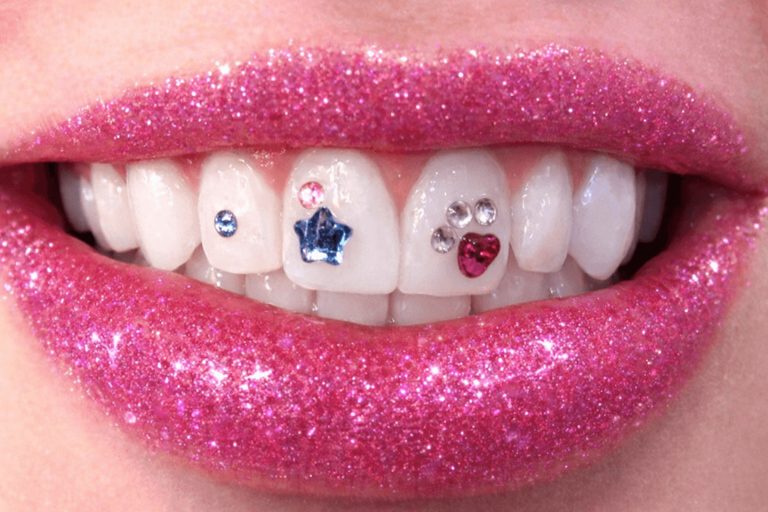 Close-up of lips with pink glitter lipstick and decorated teeth with small colorful jewel stickers.