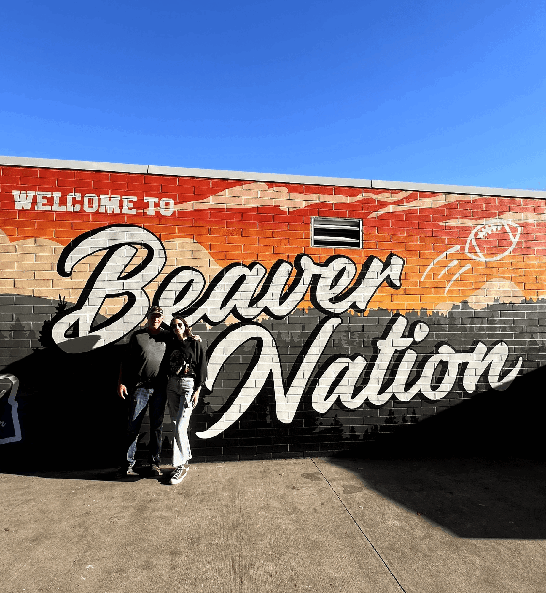 Two people standing in front of a colorful mural that says